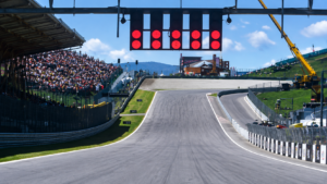 Red start lights over an empty start straight, with a packed grandstand beside the track