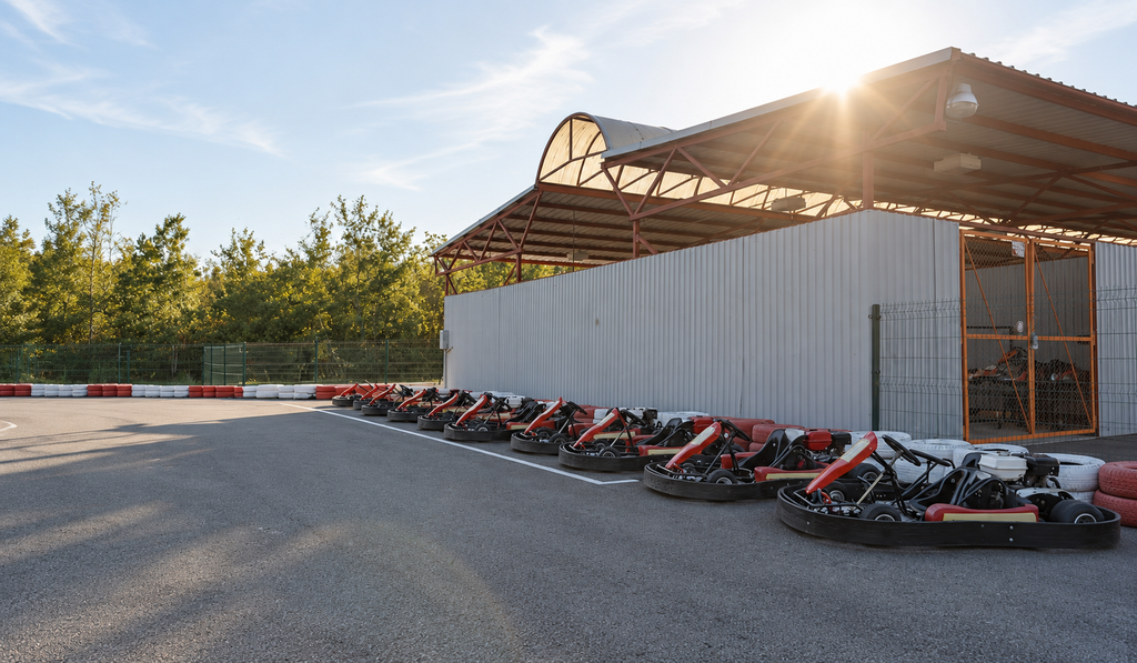 A row of racing go-karts parked beside a track and garage in daylight