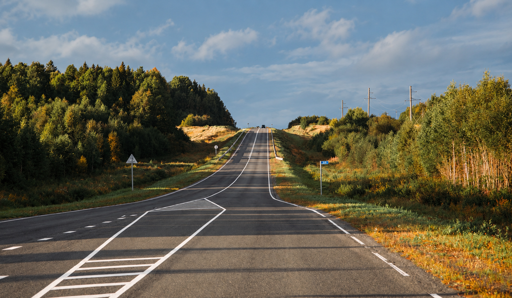 A steep empty road rising through forested hills toward a blind crest